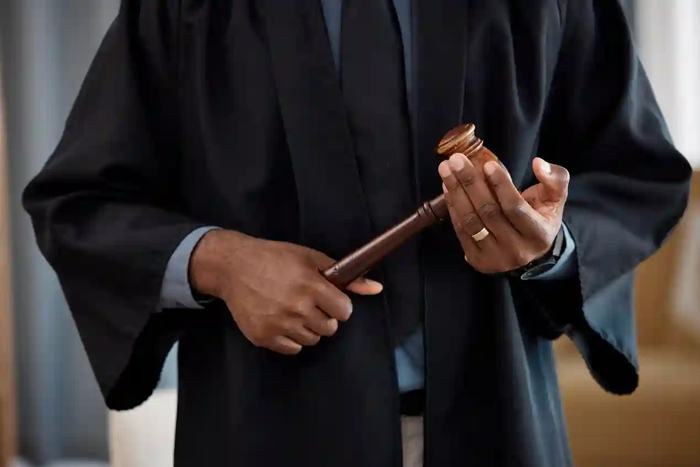 Close em mãos de um magistrado ajustando o martelo judicial antes do uso, com toga escura e ambiente sóbrio ao fundo, transmitindo a ideia de controle, análise e rigor na aplicação da Lei anticorrupção, onde cada decisão carrega peso histórico, impacto econômico e consequências práticas para quem atravessa os limites do aceitável.
