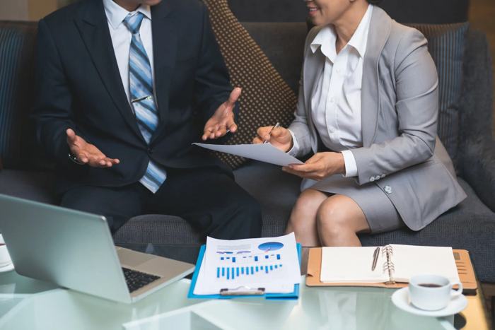 Profissionais discutindo documentos com gráficos financeiros em reunião de negócios, simbolizando compliance em licitações e práticas de integridade.