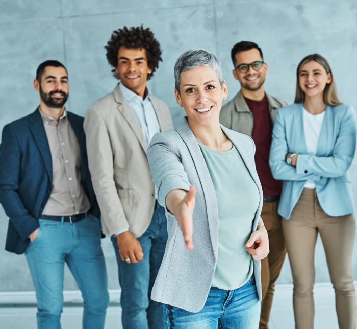 Grupo de profissionais sorrindo, com uma mulher em destaque estendendo a mão, simbolizando boas-vindas e oportunidades no contexto da contratação temporária na administração pública.