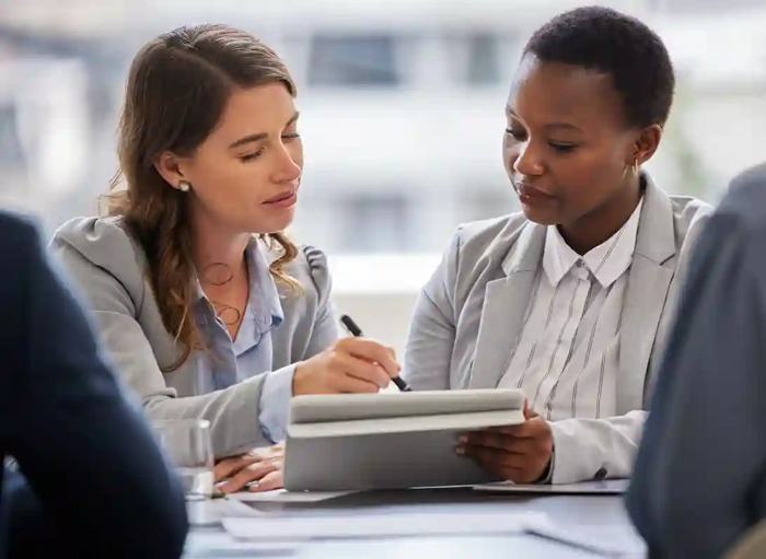 Reunião profissional entre duas gestoras analisando documentos digitais em processo de gestão de contratos administrativos.
