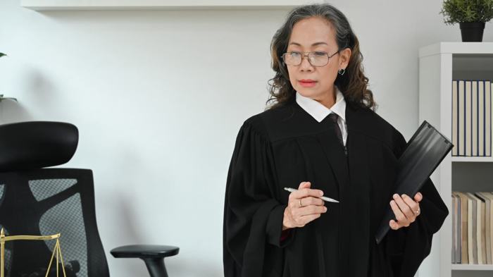 Mulher vestida com toga preta, segurando uma pasta e uma caneta em um ambiente de escritório. Representação de uma autoridade fiscalizadora, simbolizando o papel do Tribunal de Contas na fiscalização dos recursos públicos.