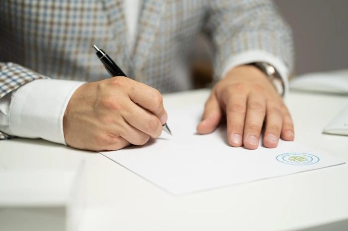 Mãos de um profissional assinando documento sobre a mesa, simbolizando análise documental e comprovação de qualificação técnica em licitações.
