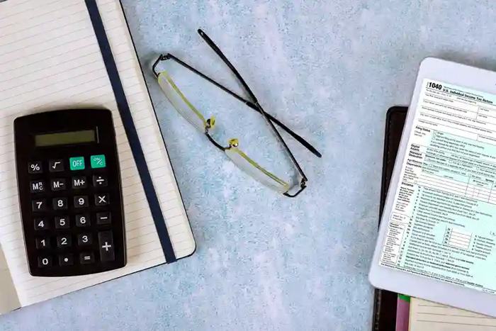 Calculadora repousa ao lado de caderno e óculos sobre mesa clara, enquanto documentos fiscais sugerem decisões estratégicas diante da Reforma tributária em 2026.